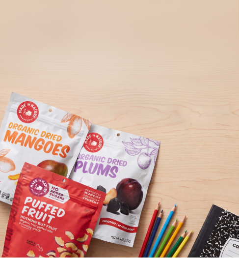 Three bags of dried fruit on a wooden surface with school supplies.