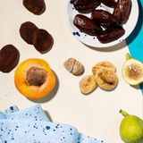 Assorted dried fruits including dates, apricots, figs, and a lemon on a light background.